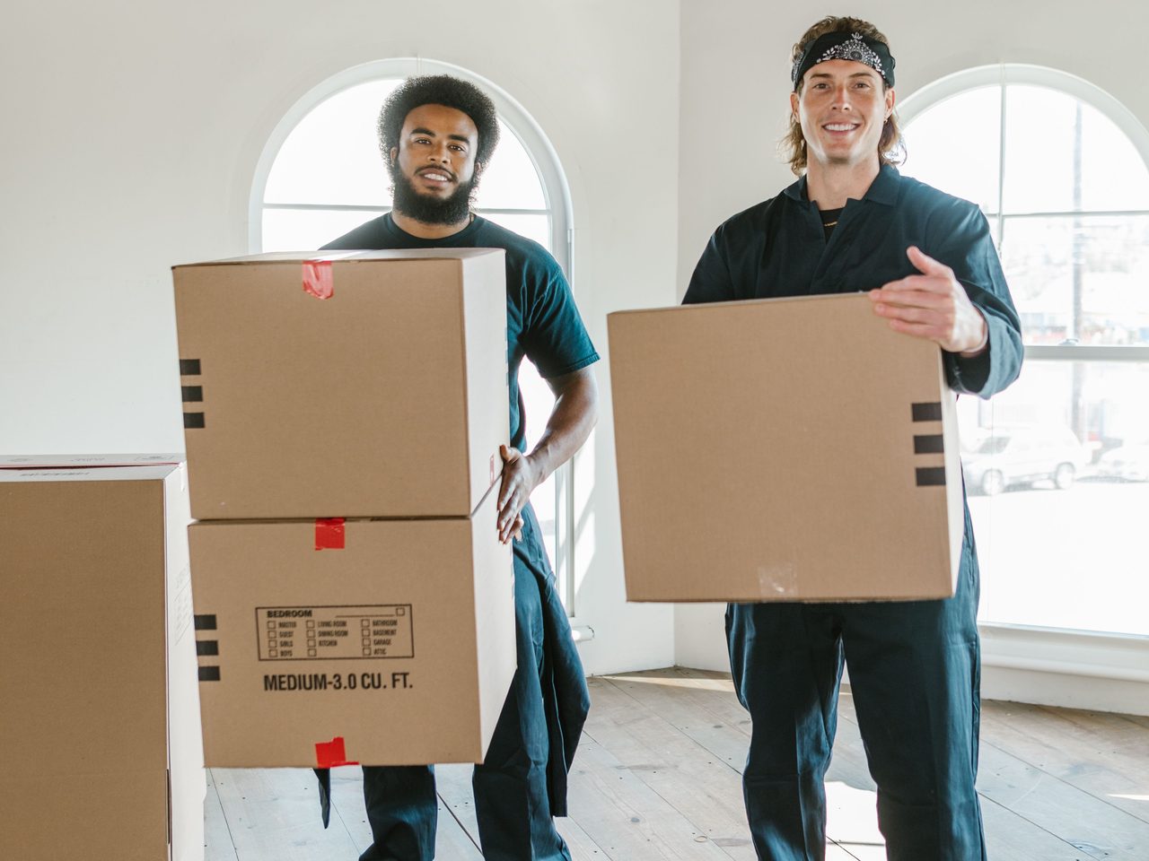 Two movers carrying boxes into an empty room on moving day
